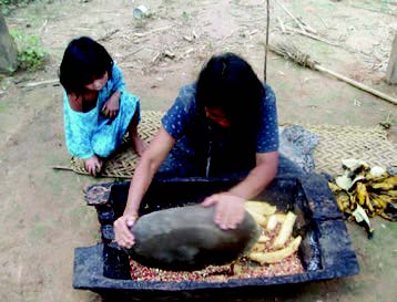 Figure 5. Tsimane woman and child crushing dried corn with large stone.